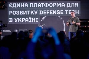 「ウクライナのdefense tech発展のための単一プラットフォーム」と書かれたスクリーンの前で登壇者が話している。手前に観客の後ろ姿