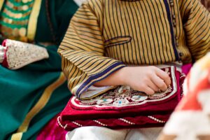 金糸で花の文様を刺繍した赤い布製の袋を、伝統衣装を着た子どもが手にしている
