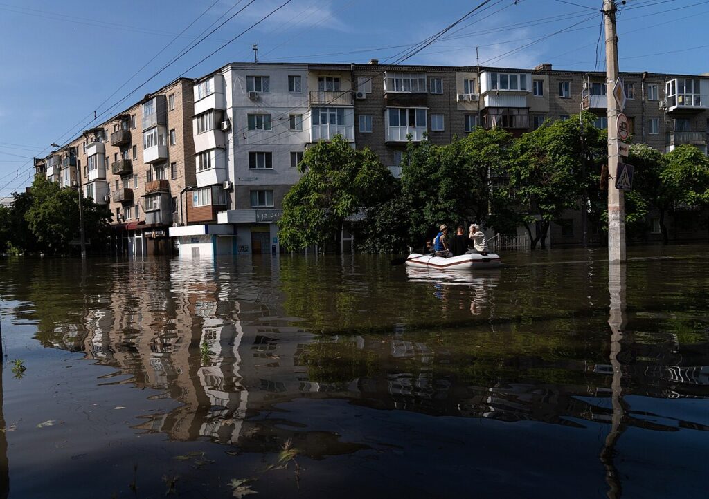 A rubber boat carrying people passes in front of a flooded apartment building