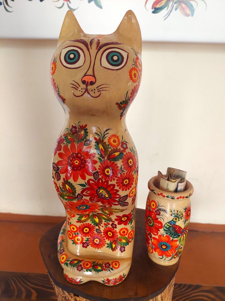 A wooden cat figurine painted with a floral pattern, covered in flowers rendered in the Petrykivka technique