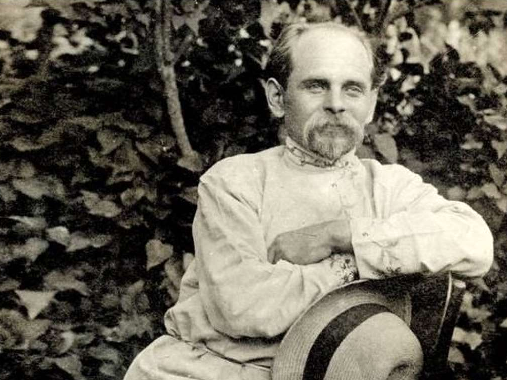 A mustached man in an embroidered shirt, seated