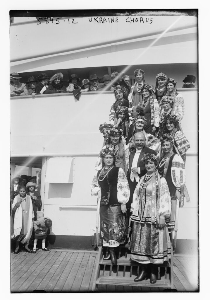 Black-and-white photograph of choir members in folk costume lined up on a ship's gangway