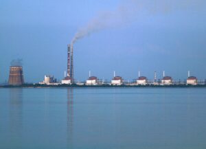 貯水池の対岸に並ぶ原子炉建屋と冷却塔、火力発電所の煙突