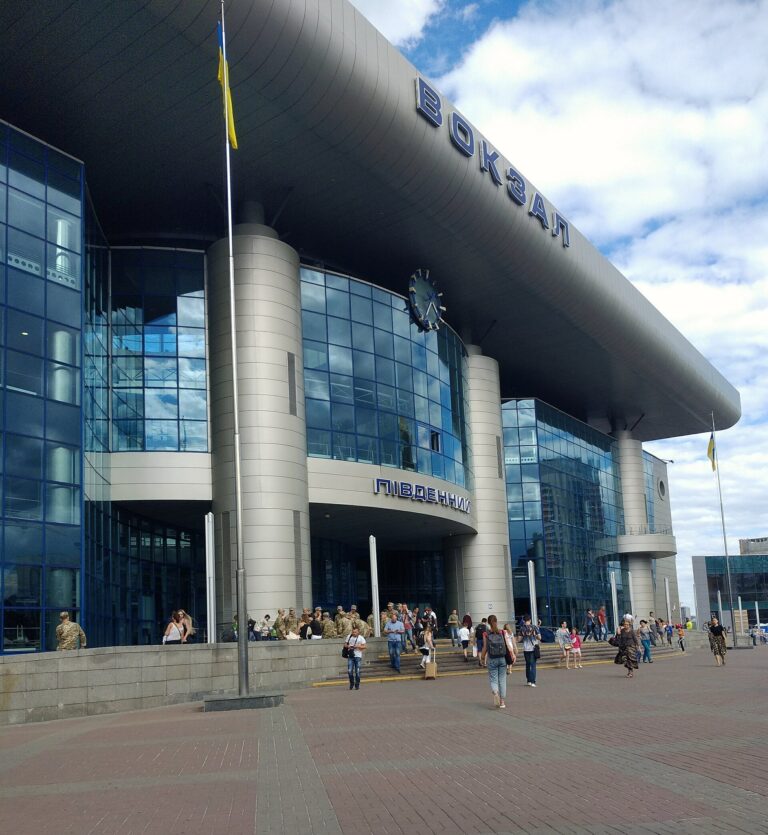 「ВОКЗАЛ ПІВДЕННИЙ」と書かれたキーウ中央駅(南駅)の玄関。ウクライナ国旗と、駅前を行き交う人・軍人の姿