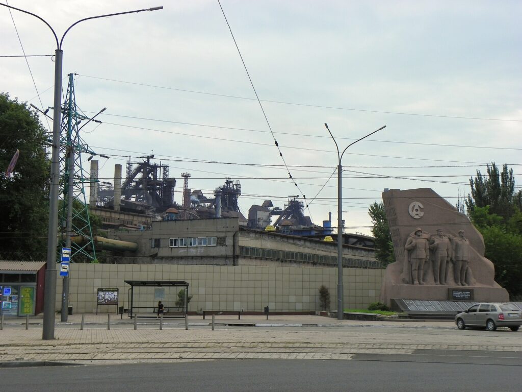 Комбінат «Азовсталь» із рядами доменних печей і трубопроводів. На передньому плані — військовий меморіал